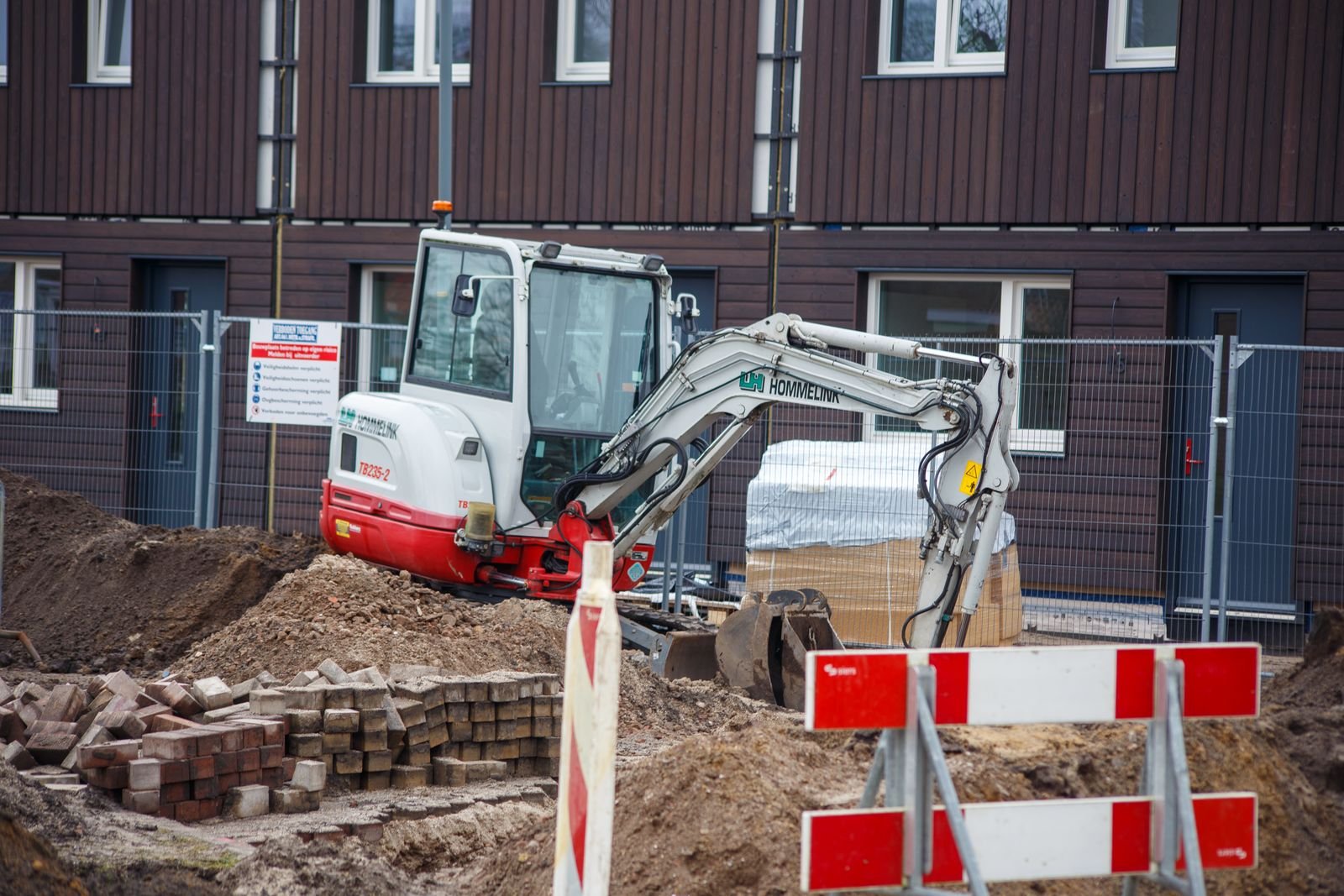 Mini-pelle qui excave le périmètre d’un immeuble en brique pour imperméabiliser la fondation par l’extérieur, chantier résidentiel dans la région de Montréal
